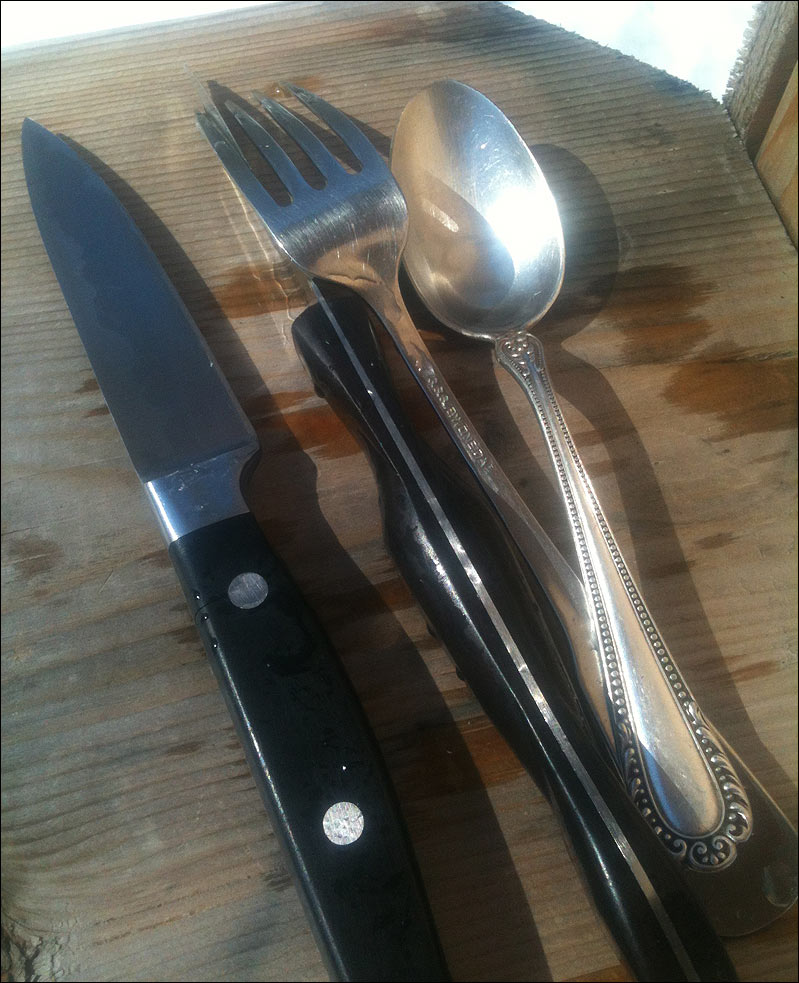 Clean utensils - two knives, a fork, a spoon, drying in the sun.